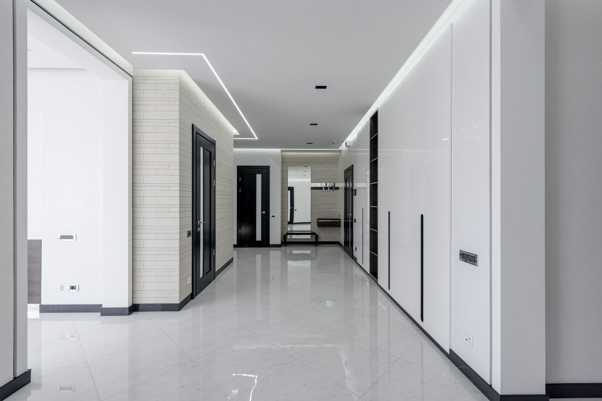 Spacious corridor of modern apartment with white walls dark doors and LED highlighting on ceiling